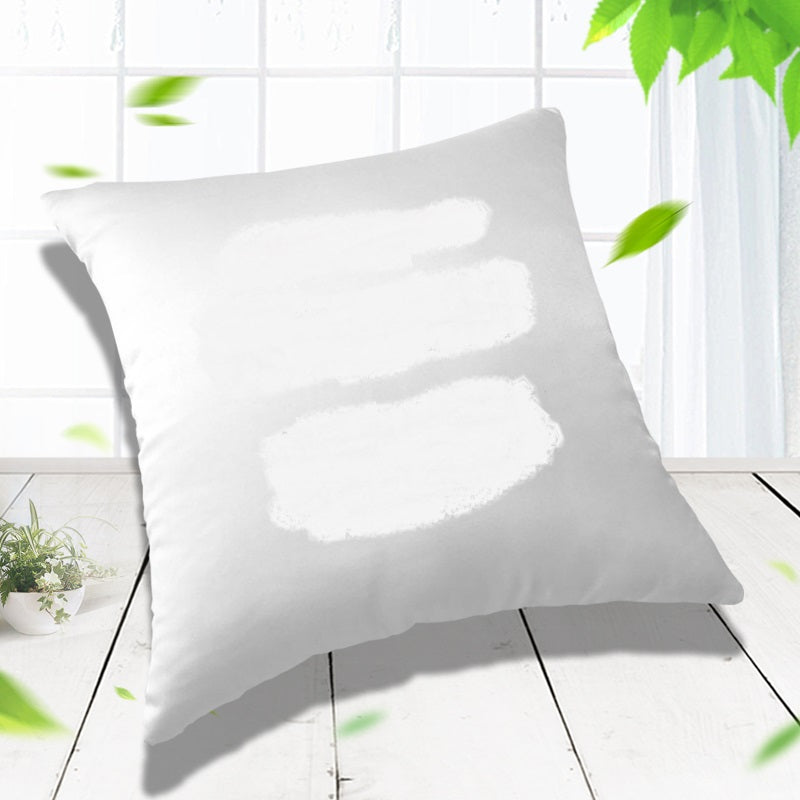 White pillow-cover example with white brush marks masking its front, displayed beside a window.