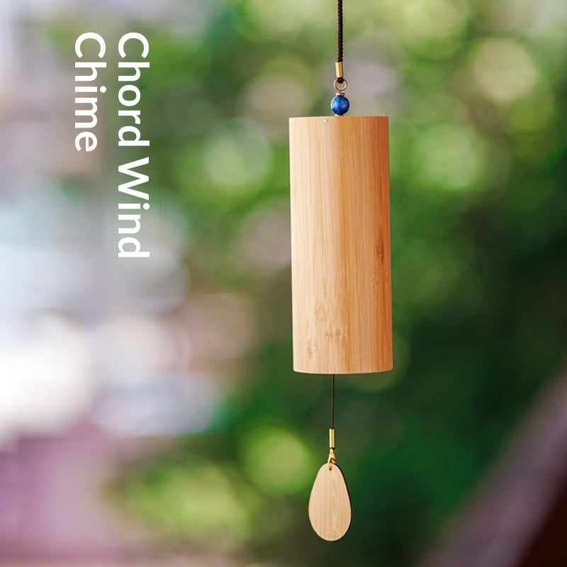 Cylindrical bamboo wind chime with a teardrop-shaped hanging piece against a green background.