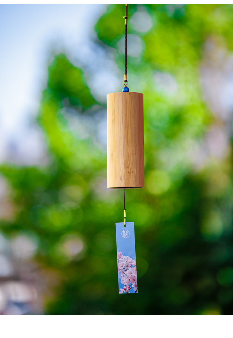 Bamboo wind chime with a floral paper hanging strip outdoors.