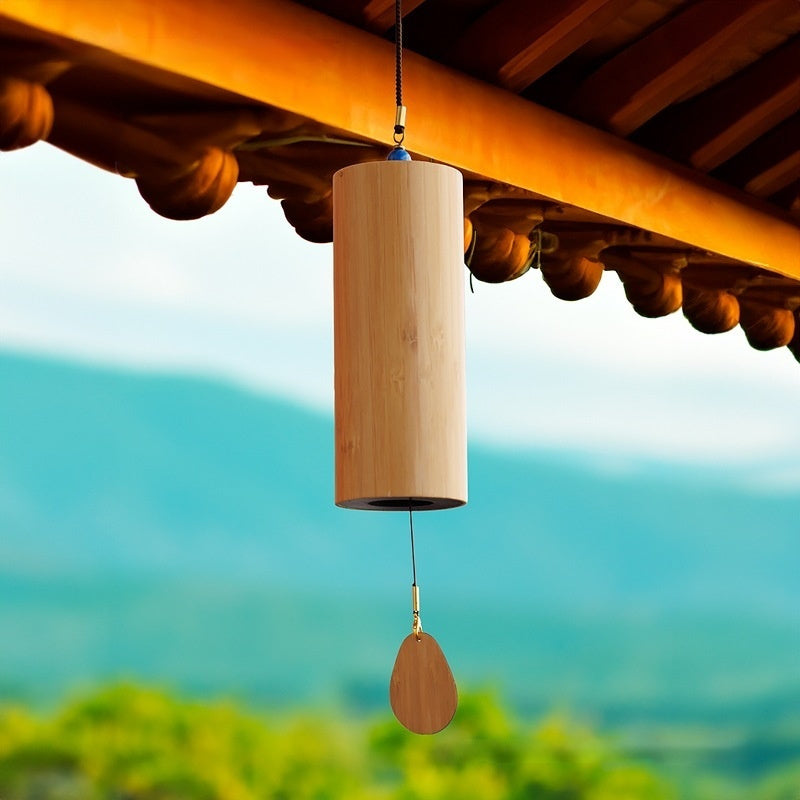 Cylindrical bamboo wind chime hanging beneath a wooden roof.