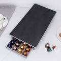 Silver-gray coffee capsule drawer shown open with a black top; coffee capsules and tableware are display props, not included